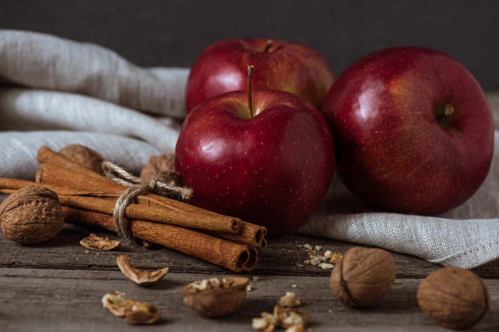 Apples and cinnamon sticks gathered on a table and cloth.